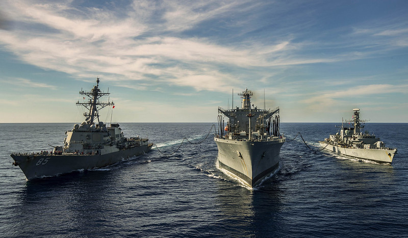 Photograph showing three navy ships coming towards the camera on a dark blue sea with bright blue sky and wispy white clouds above.